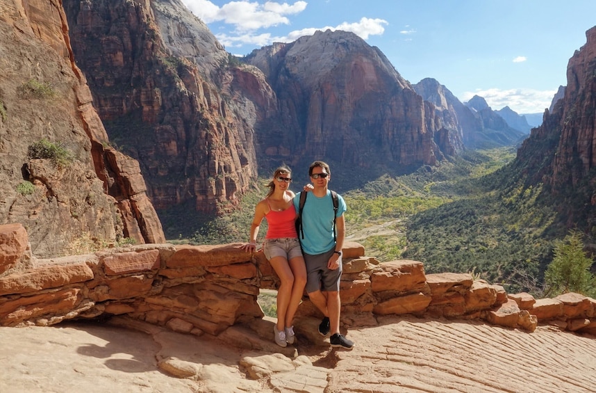 Two people standing on a rocky ledge with a canyon in the background. 1