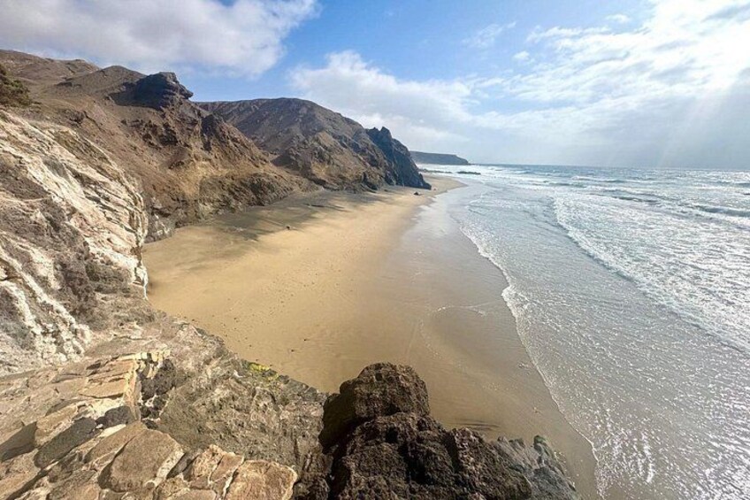 A coastal landscape with a sandy beach, rocky cliffs, and waves. 4