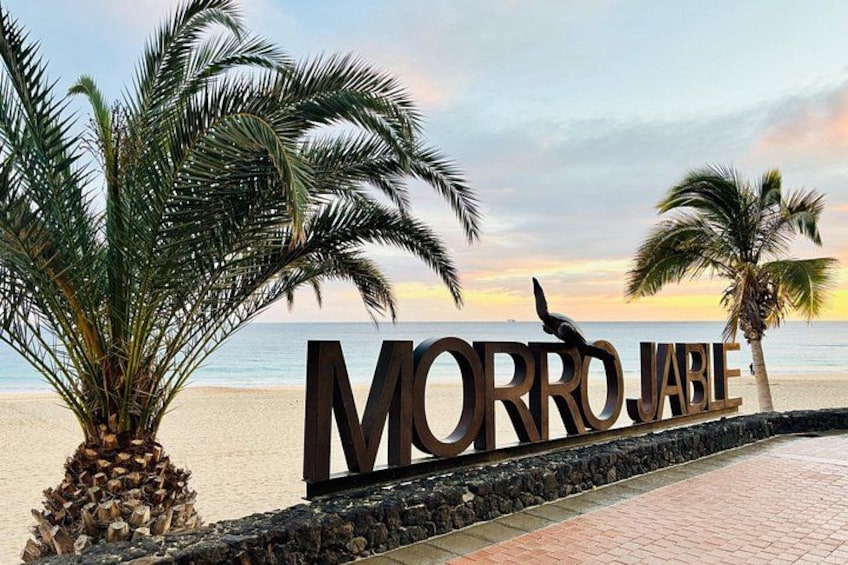 Een strand met palmbomen en een bord waarop 'MORROJABLE' staat. 2
