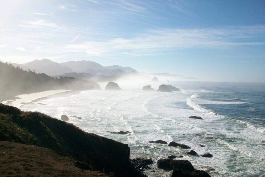 A coastal landscape with waves, rocky shore, and distant mountains. 4