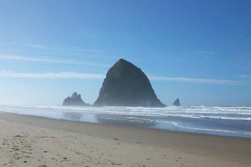A beach with a large rock formation and waves. 3