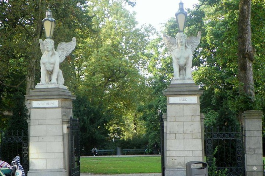 L'ingresso di un parco con due statue di putti su piedistalli, un lampione e un cancello in ferro battuto. 2