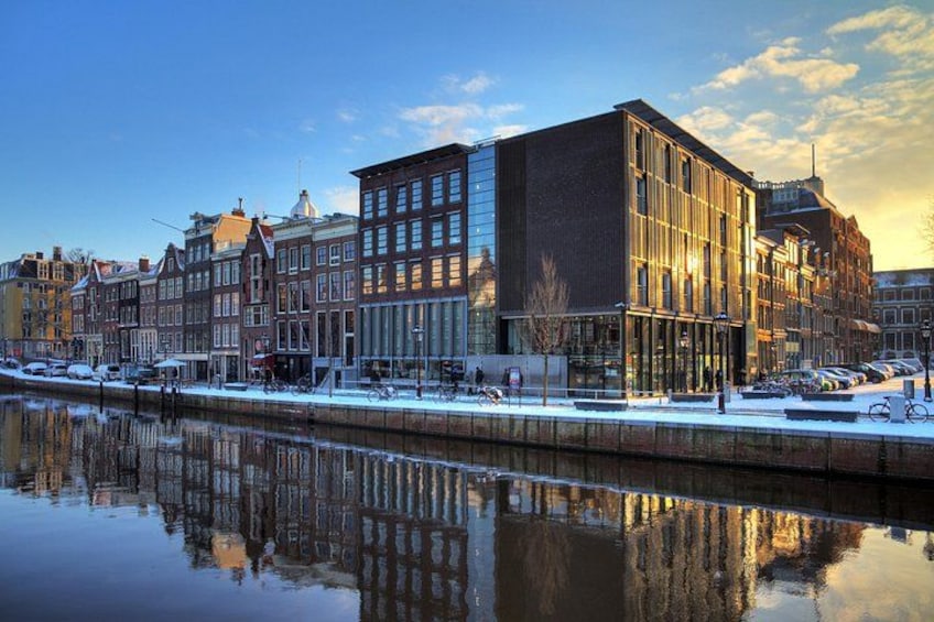 Un canale con edifici riflessi nell'acqua, cielo sereno e alcune persone che passeggiano. 3