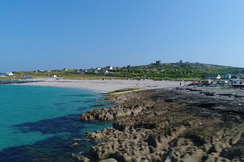 A coastal landscape with clear turquoise waters, rocky shoreline, and a distant hill with structures. 3