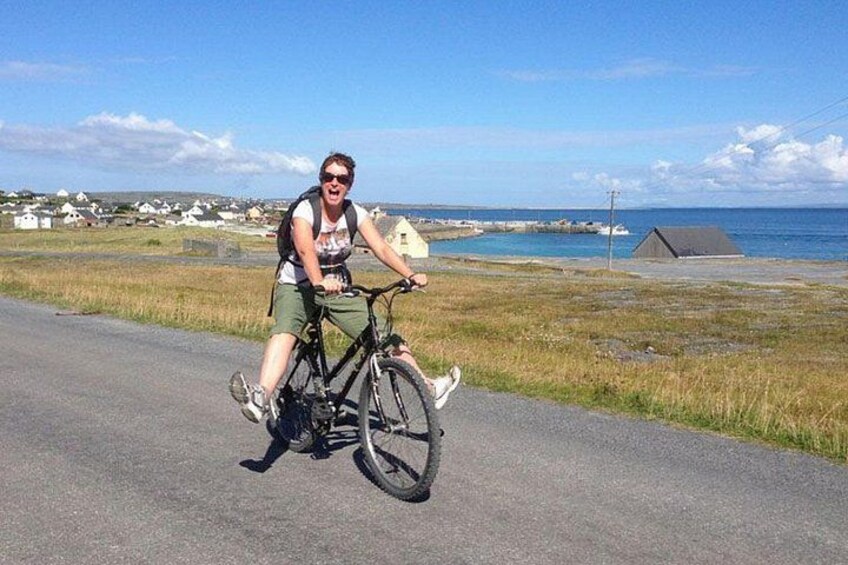 A person riding a bicycle on a paved road with a coastal landscape in the background. 2