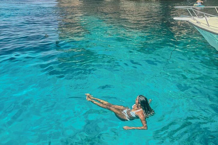 Una persona flotando en aguas azules cristalinas con un bote al fondo. 2