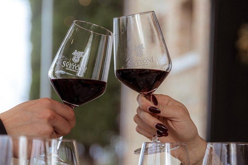 Two hands holding wine glasses with a vineyard logo, toasting with a glass of red wine. 5