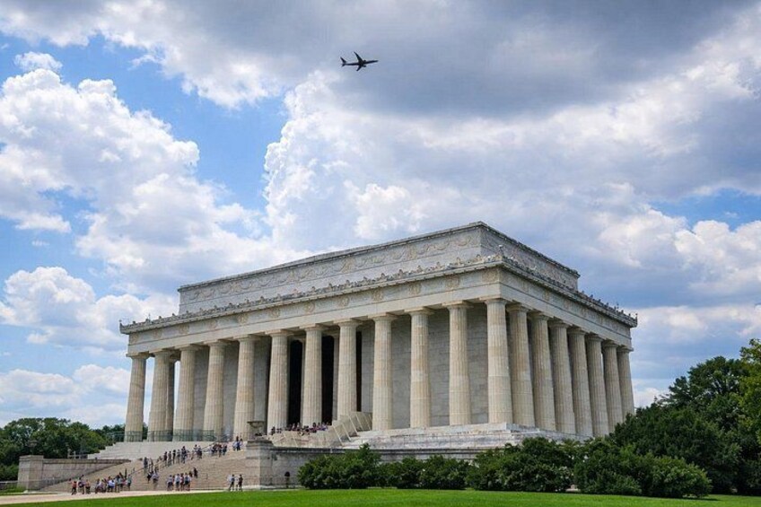 The Lincoln Memorial with columns, steps, and a plane in the sky. 2