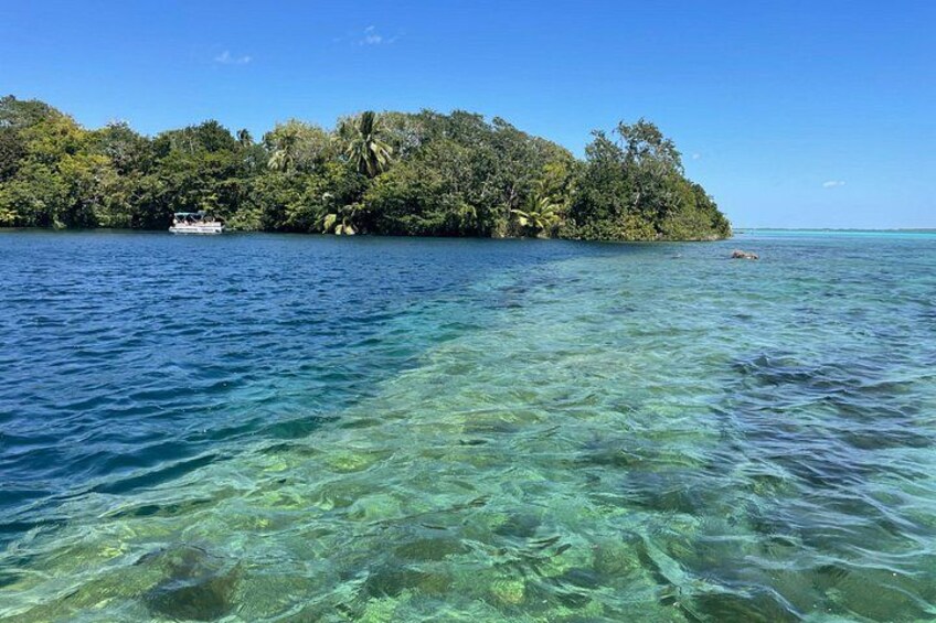 Mar tropical cristalina con un barco pequeño y una isla exuberante al fondo. 1