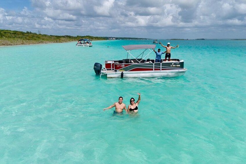 Un bote con gente navegando en aguas turquesa cristalinas, una costa distante y otro bote al fondo. 2