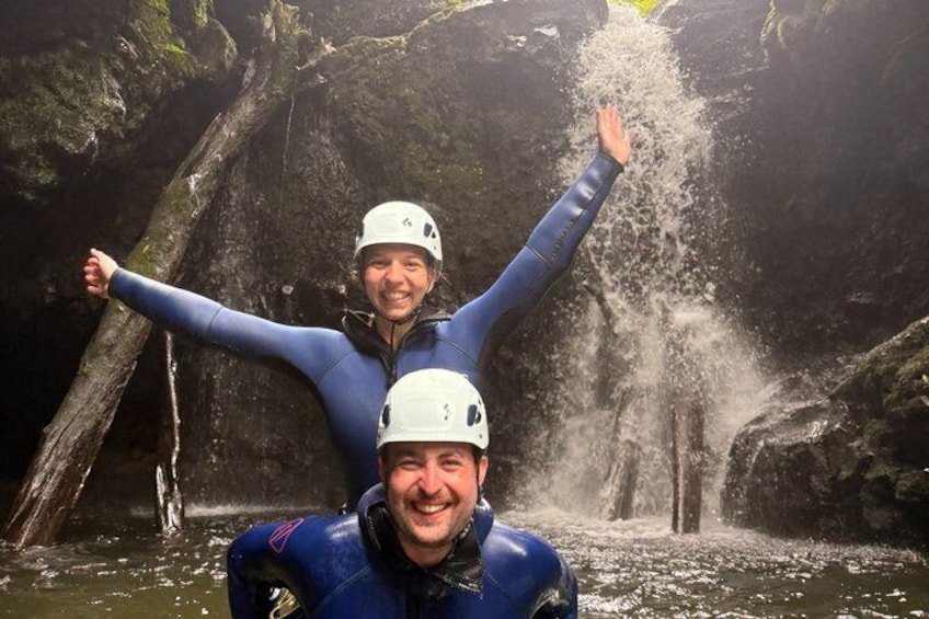 Twee mensen in blauwe neopreenpakken en witte helmen staan voor een waterval. 3