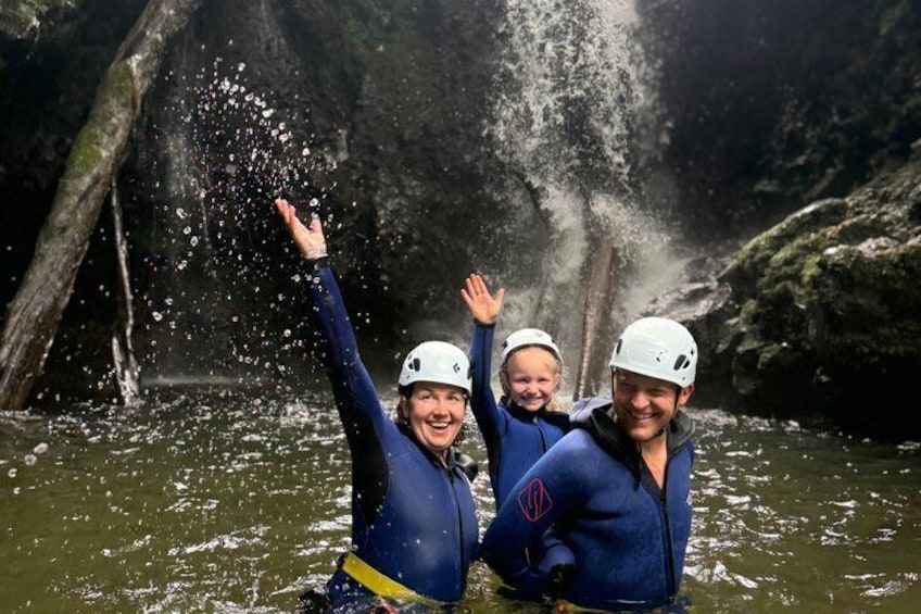 Drie mensen in een rivier, uitgedost in helmen en neopreenpakken, met een waterval op de achtergrond. 4