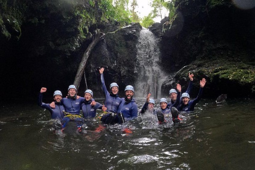 Un grupo de personas con trajes de neopreno y cascos de pie en un río, con una cascada al fondo. 5