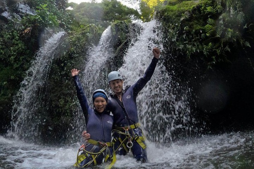 Dos personas con trajes de neopreno y cascos disfrutando de una cascada. 2
