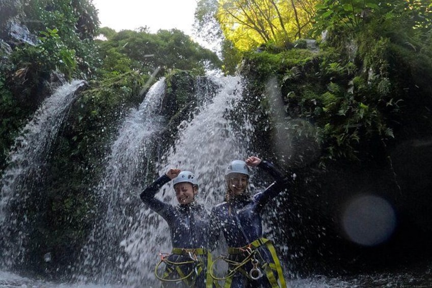 Dos personas con casco y trajes de neopreno de pie frente a una cascada. 4