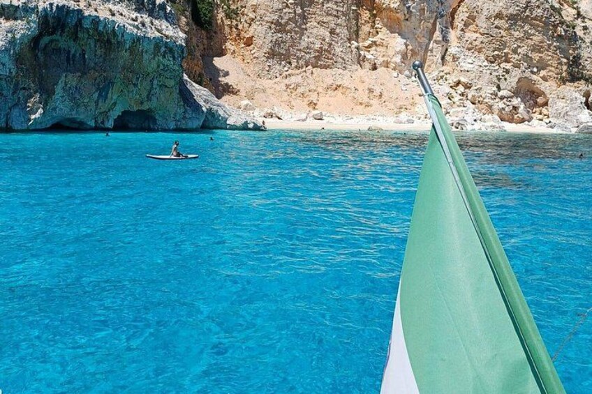 Une mer d’un bleu profond, une personne qui rame sur un petit bateau, des falaises rocheuses et une plage de sable. 5
