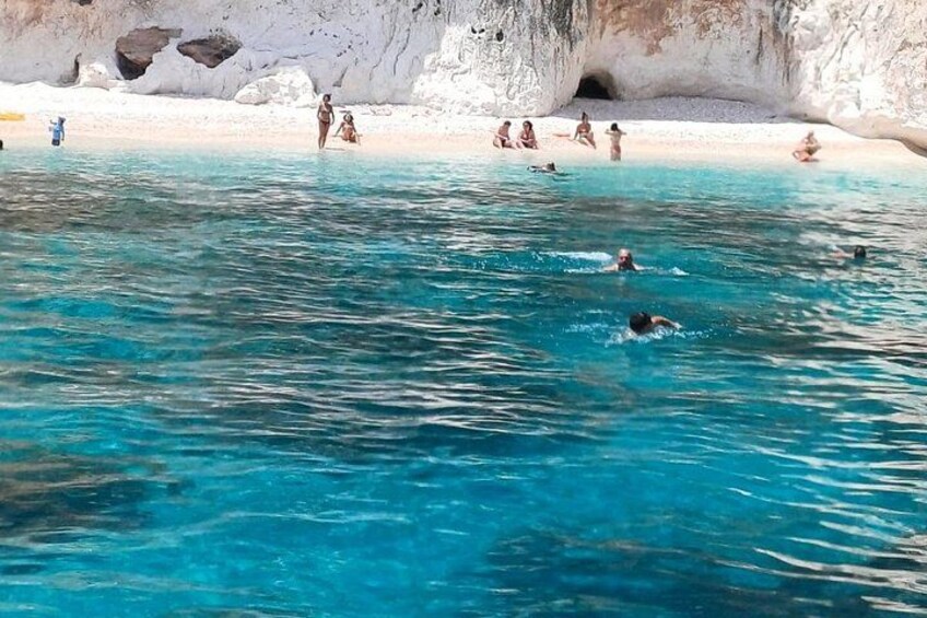 Une plage avec une eau d’un bleu limpide, des gens qui se baignent et une grotte en arrière-plan. 3