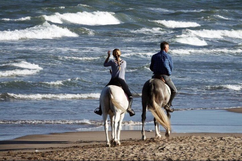 Two people riding horses on a beach with waves in the background. 2