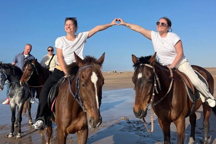 People riding horses on a beach with clear skies. 1