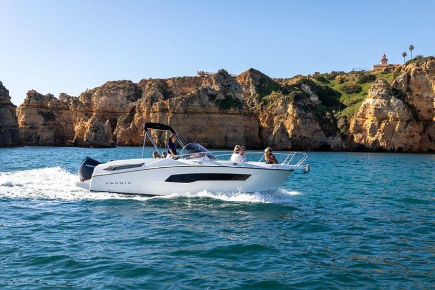 A white motorboat named 'KARRIO' on calm waters with rocky cliffs and a lighthouse in the background. 2