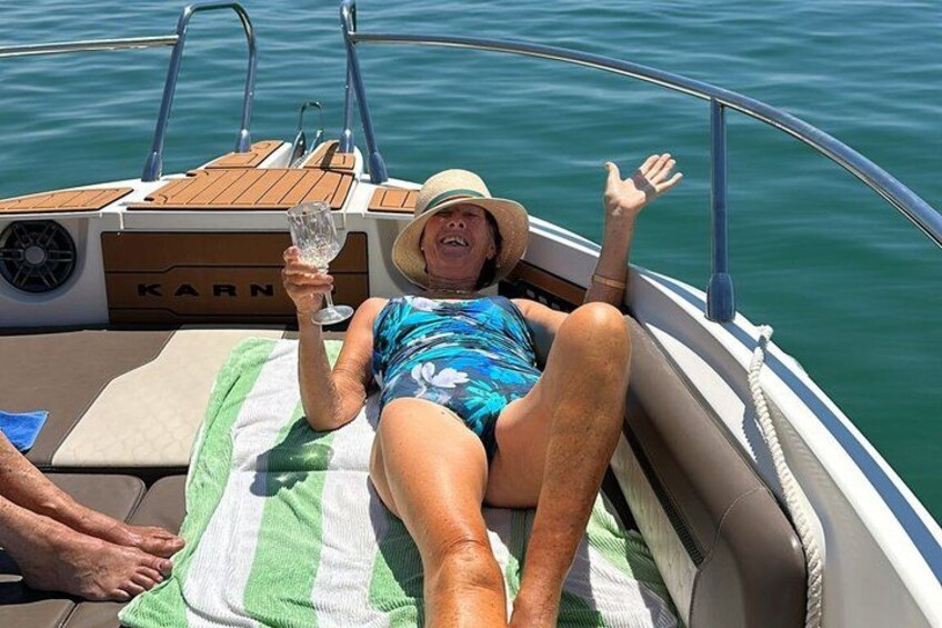 A person lying on a boat with a green and white striped towel, holding a glass of water, and wearing a blue swimsuit. 5
