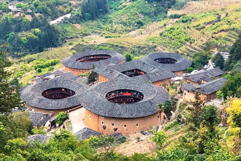Un ensemble de bâtiments traditionnels à toits arrondis, entourés d’une végétation luxuriante et de collines en terrasses. 1
