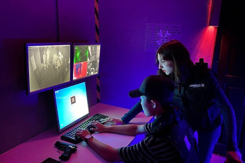 Una persona usando una computadora portátil con múltiples monitores mostrando imágenes, en una habitación con iluminación púrpura. 1