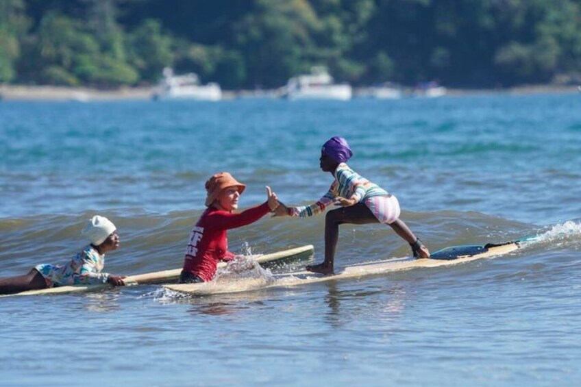 Two people on a surfboard in the water, with a boat in the background. 1