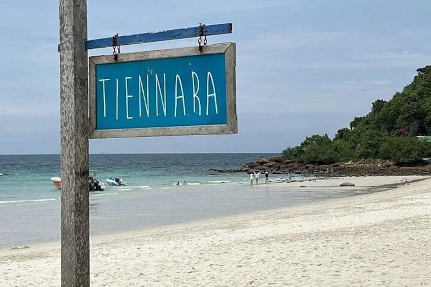 Ein Strand mit einem Schild, auf dem 'TIENNARA' steht, und einem Holzpfosten. 3