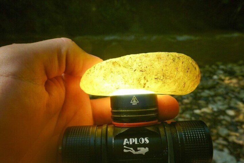 Een hand die een camera vasthoudt, met een zaklamp eraan vastgemaakt, met een rots en een wateroppervlak op de achtergrond. 3