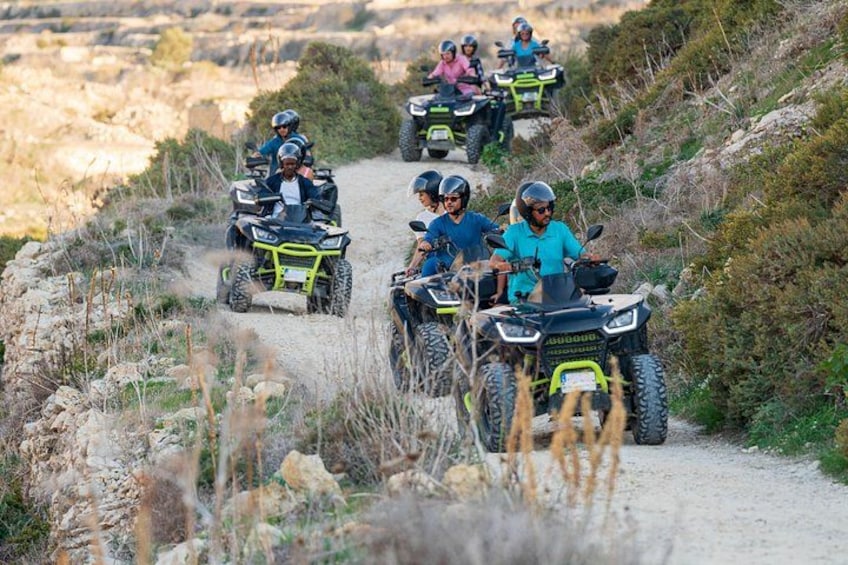 Een groep mensen rijdt op terreinwagens over een onverhard pad, omringd door dorre begroeiing en rotsachtig terrein. 1