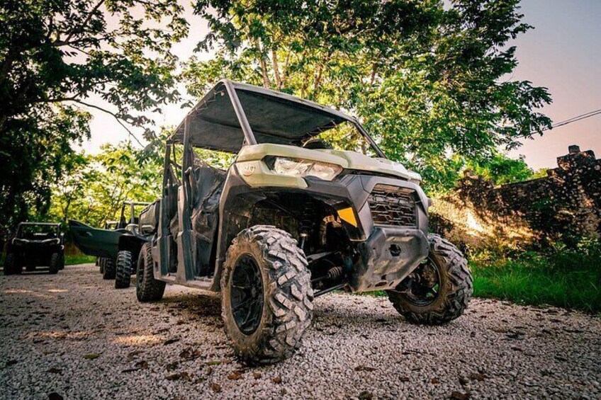 A white off-road vehicle parked on a gravel path with trees in the background. 1
