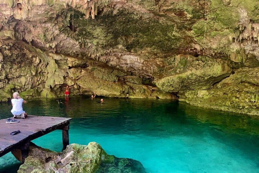 A natural pool with clear turquoise water, surrounded by rocky cliffs and a wooden dock. 2