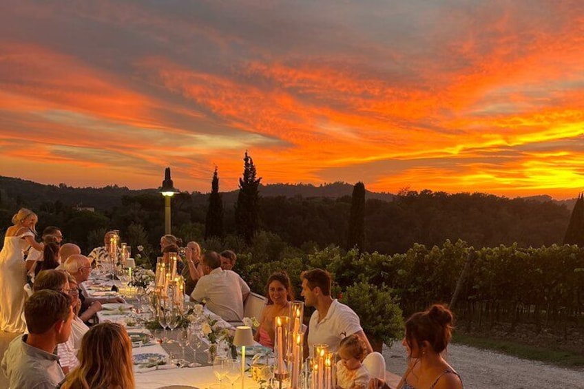 A group of people dining outdoors at sunset with a vineyard in the background. 1