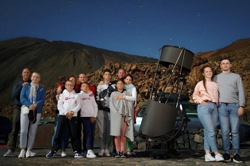 A group of people standing in front of a telescope on a rocky hillside at night. 3