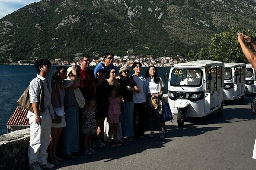 A group of people standing by a waterfront with a mountainous backdrop. 1