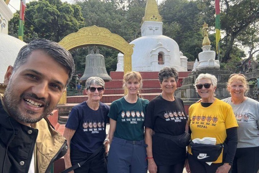 Un groupe de personnes se tient devant un temple blanc orné d’une cloche, le tout étant entouré de verdure. 5