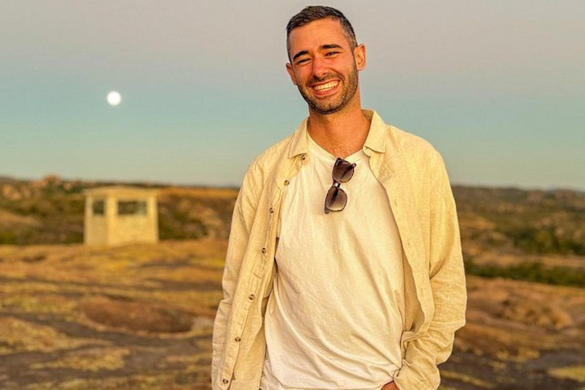 A person standing outdoors with a clear sky and a small structure in the background. 2