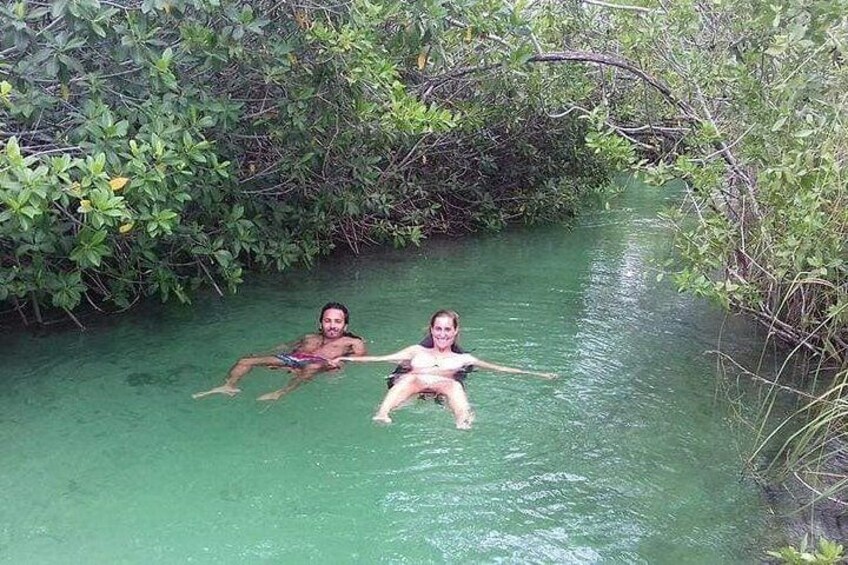 Two people floating in a greenish river surrounded by dense vegetation. 3