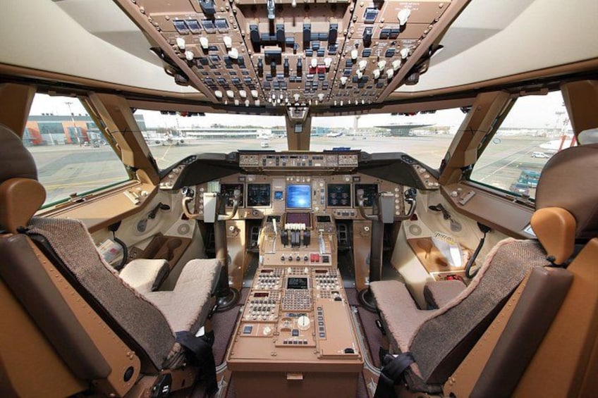 Cockpittet på et fly med flere kontrolpaneler, et stort overliggende panel og to pilotstole. 1