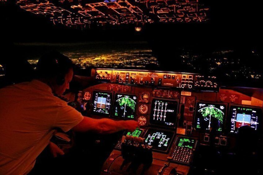 En person betjener et flycockpit med flere oplyste skærme og betjeningsknapper. 5