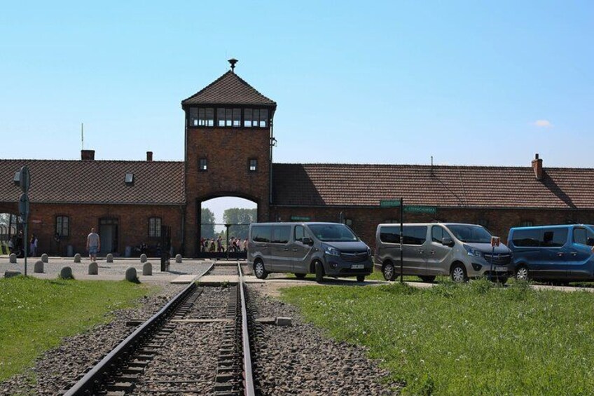 A historical building with a watchtower, a train track, and several parked vehicles. 4