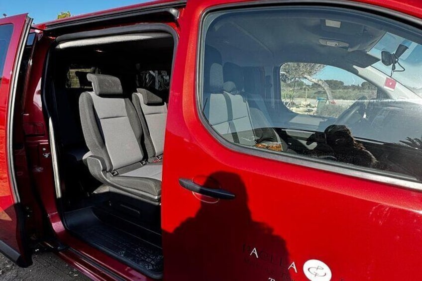 A red van with its door open, revealing the interior seating and a dog in the back. 2