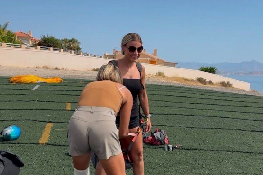 A person in a black top and beige shorts bending over on a green field with a blue ball nearby. 5