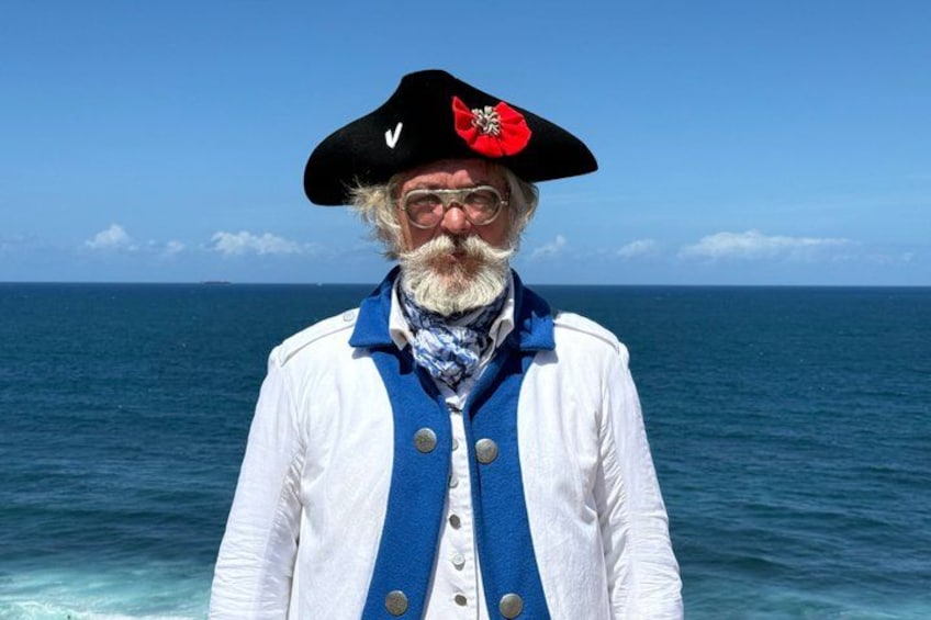 A person in a white coat and blue vest standing by the ocean. 1