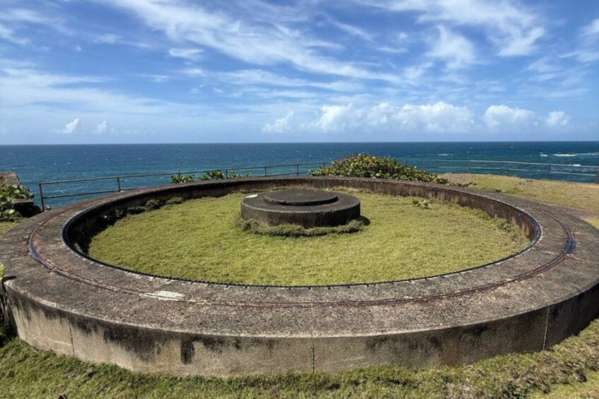 A circular concrete structure with a grassy center, surrounded by a metal railing, overlooking the ocean. 2