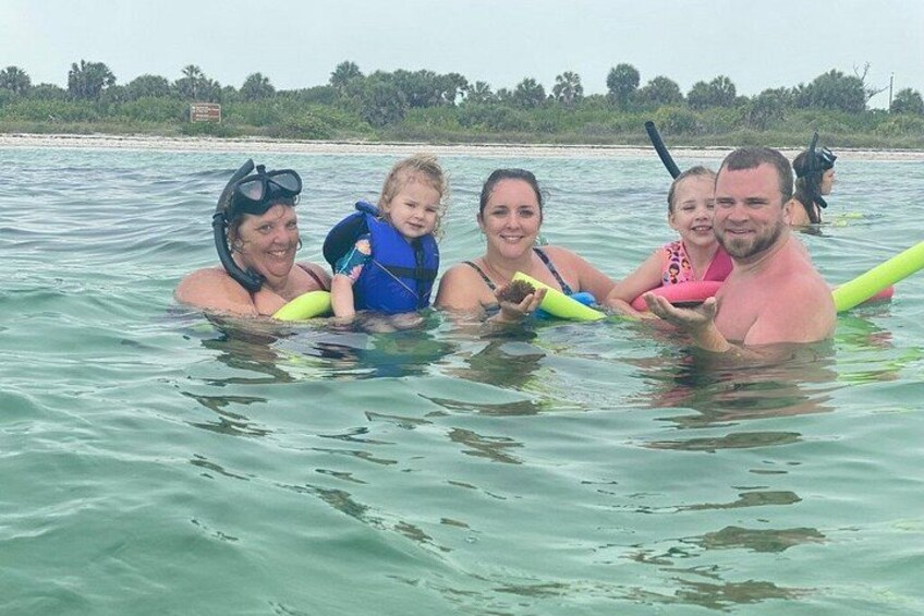 Un grupo de personas en el agua, algunas con equipo de snorkel, con una playa y vegetación al fondo. 4