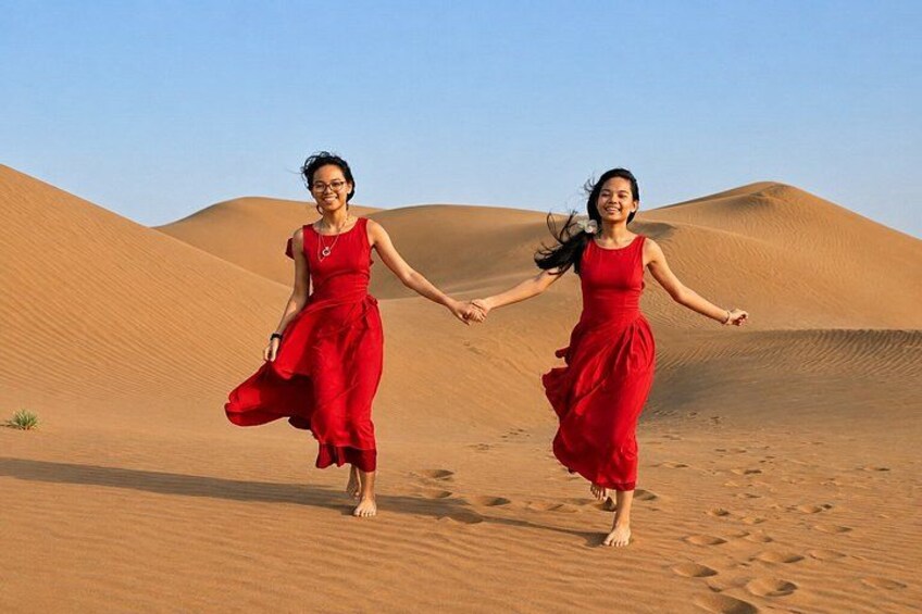 Two people in red dresses running on a sandy beach with dunes in the background. 2