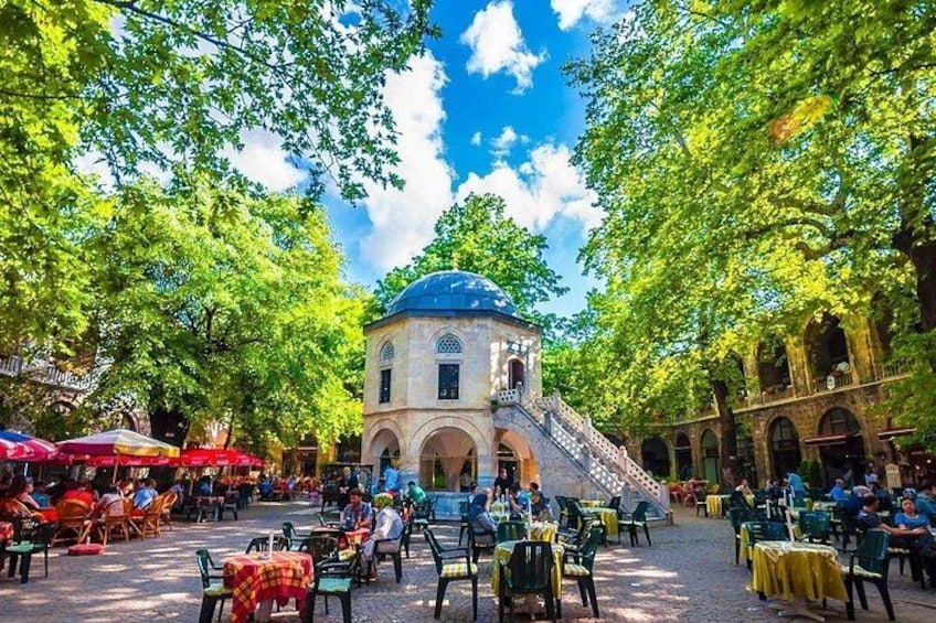 Une cour avec des espaces de repos en plein air, un bâtiment central surmonté d’un dôme et des arbres. 1