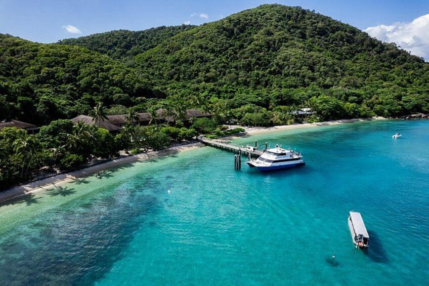 Une zone côtière aux eaux turquoise et limpides, un bateau amarré à un quai, et une colline verdoyante en arrière-plan. 5